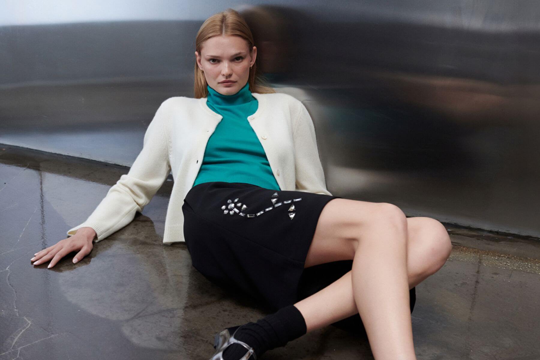 Model is leaning down on floor in embroidered arielle pocket short and cashmere creme cardigan layered over teal james sleeveless turtleneck.