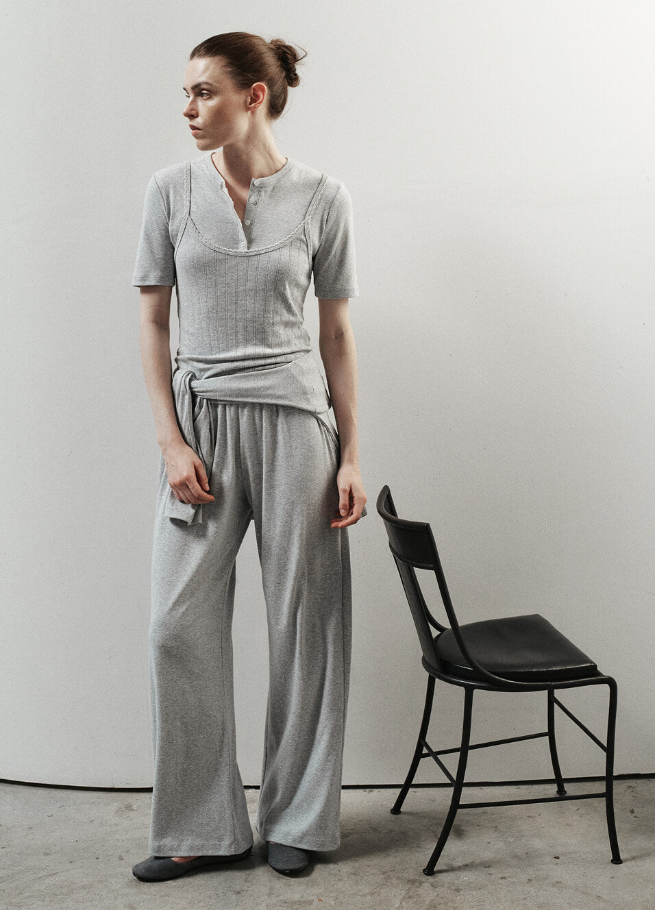 Woman standing in light grey melange next to chair.