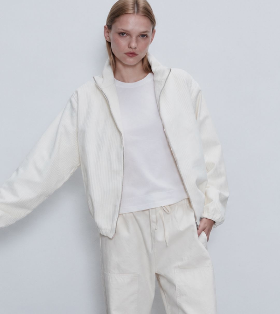 Model is standing holding metal chair in white tee and sammi corduroy set in creme.