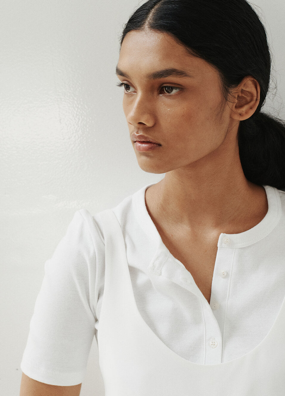 Close up of woman in white button down tank and shirt, looking to the side.