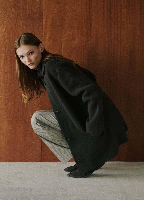 Model is squatting down in zoe sweater jacket and pinstripe pants.